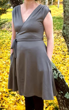 Load image into Gallery viewer, Wrap dress in olive colour on a live model. No head or legs, just the dress. Model has hands in the side seam pockets. Model is standing next to a tree, back ground is yellow because of fallen autumn leaves.