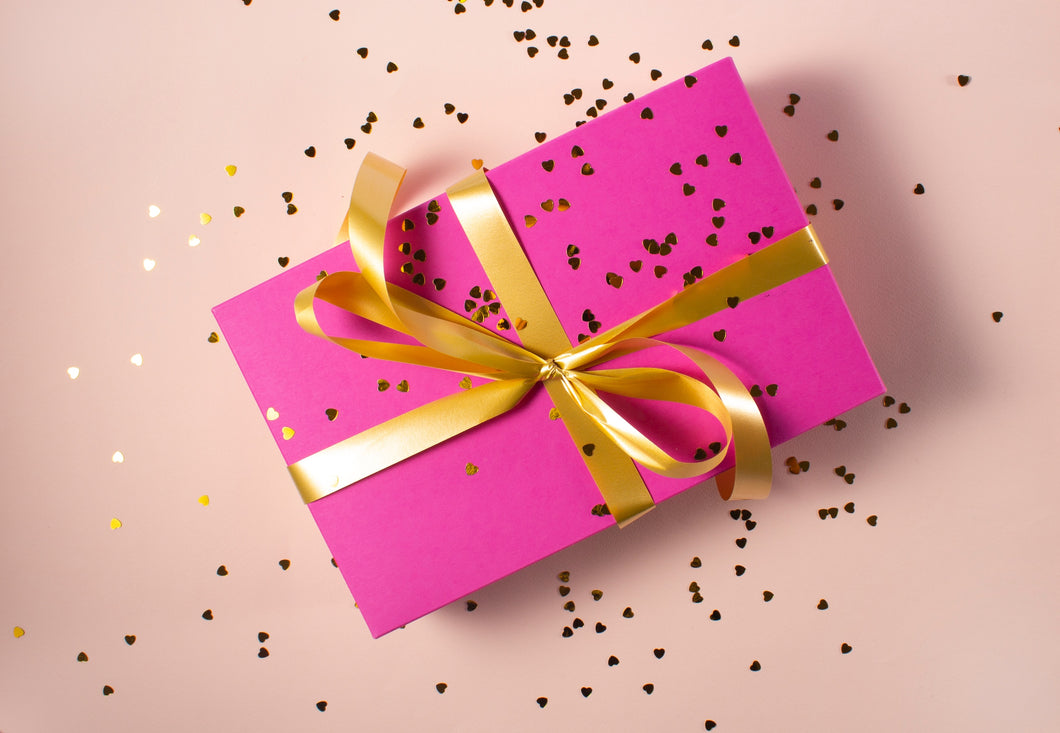 Picture illustrating the idea of the gift card. A gift wrapped in pink paper with a golden ribbon and golden sparkles around. Light background.